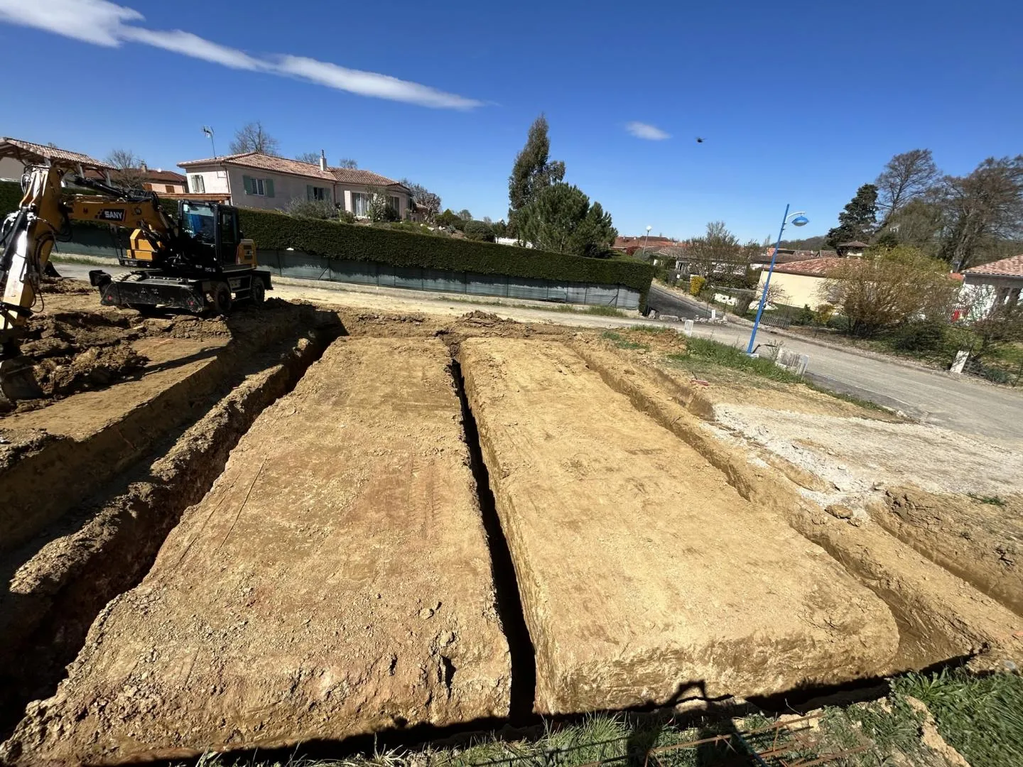 vue d'un terrain excavé par une entreprise de terrassement avec une pelleteuse à proximité, préparation pour travaux de fondation